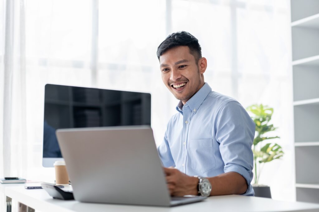 An,Adult,Asian,Man,Smiles,While,Working,On,His,Laptop